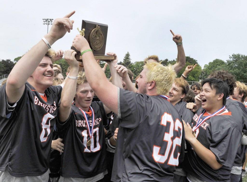 Portland Press Herald photo by John Ewing 
 Brunswick co-captain Max Gramins holds aloft the Class B boys lacrosse state championship plaque after the Dragons sank Greely in overtime Saturday in Portland.