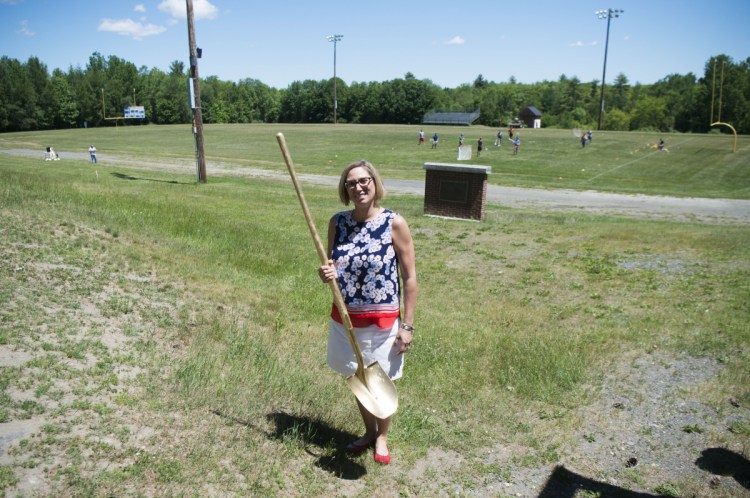 Lisa Burton, president of the Messalonskee All Sports Boosters and a leader of the effort to replace Messalonskee High School's outmoded track and football field, behind her, with an eight-lane track and an all sports turf field, stands ready with a ceremonial gold shovel Friday for the groundbreaking at the complex.