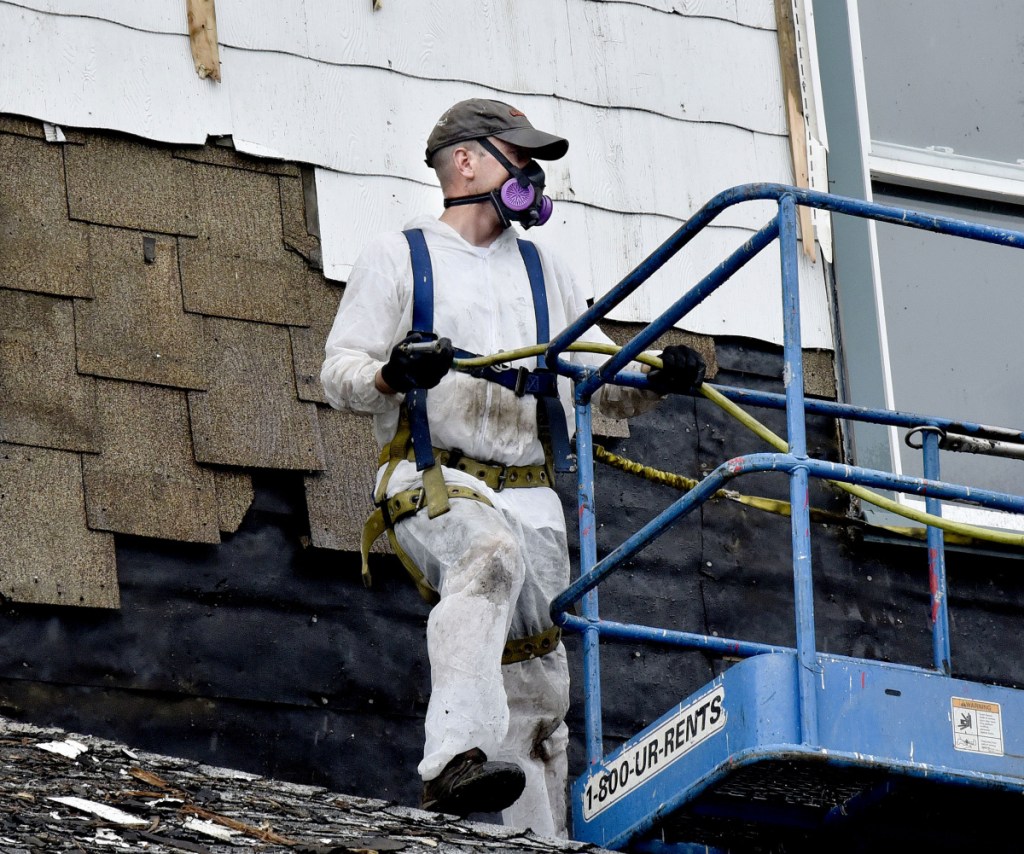 Eben Henderson wears a respirator while tearing off siding on the historic Kennebec Valley Inn in Skowhegan on Monday.