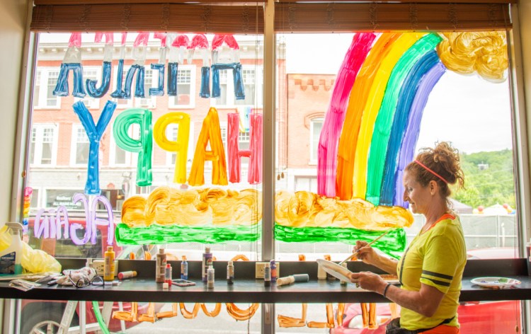 Lynne Violette, of Manchester, paints the window of Mulligan's in Hallowell on Saturday. The newly opened sandwich shop created the painting in celebration of Hallowell LGBTQ Pride.