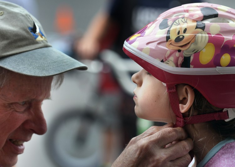 Robert McChesney secures Sophie Moore's bicycle helmet Sunday during the rodeo held at the Richmond Police Department for young riders in the community.