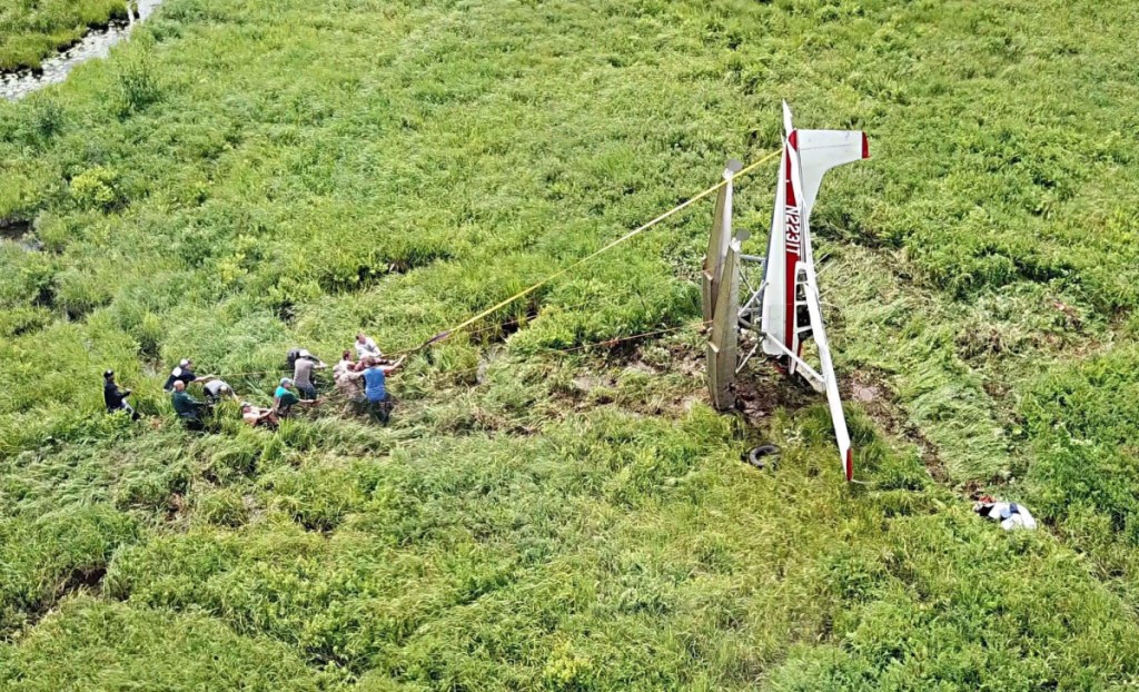 About a dozen men work to flip the crashed plane right-side up before pulling it to Route 126 on Sunday.