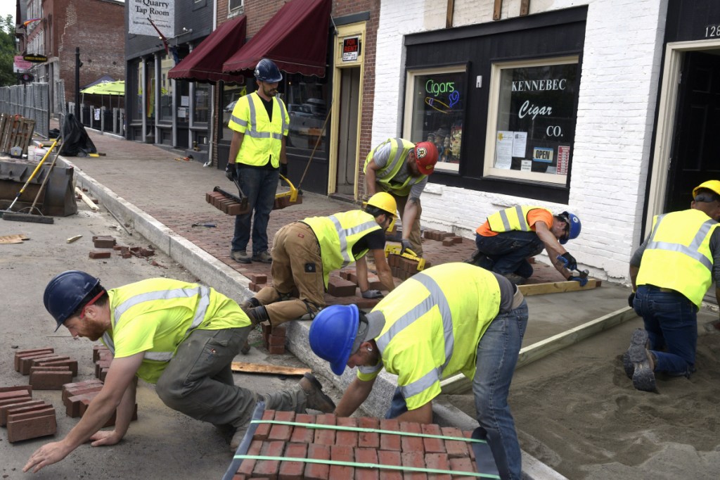 Masons lay bricks on the new sidewalk along Route 201 in downtown Hallowell on Monday as part of a large reconstruction project. Officials say this and other projects won't be affected by political wrangling over voter-approved bonds intended to pay for road construction.