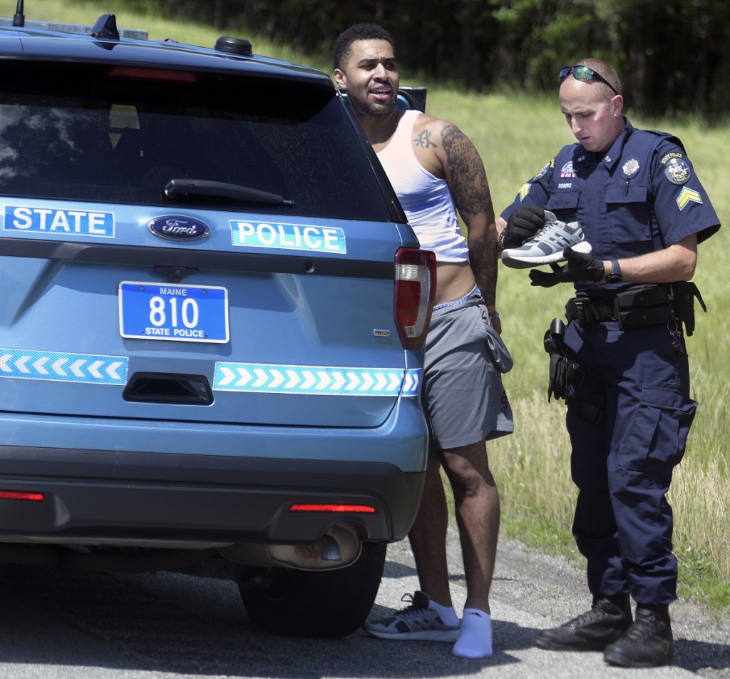 State police Cpl. Chris Rogers examines the clothes of Lenwood Williams, who was arrested Friday on the Maine Turnpike after a pursuit on the highway.