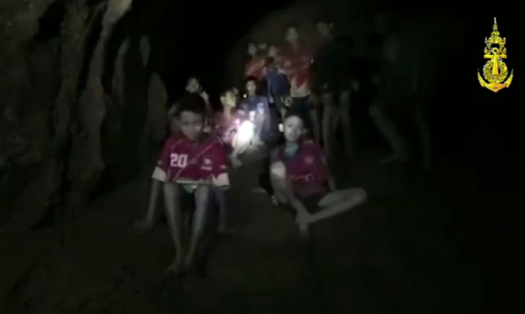 In this image taken from video provided by the Thai Navy Seal, the boys and their soccer coach sit in a cave in Chiang Rai in Thailand on Monday. The challenge now is to get them out.