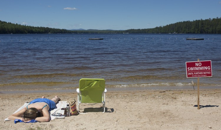 Naples resident Christy Dow sunbathes Saturday on Woods Pond Beach in Bridgton, where a number of people reported falling ill after being in the water last week.