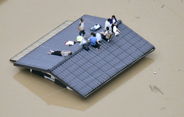 People wait to be rescued on the top of a house almost submerged in floodwaters caused by heavy rains in Kurashiki, Japan.