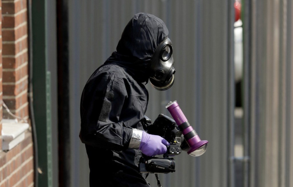 A specialist team member in a police protective suit leaves the front entrance of the John Baker House for homeless people in Salisbury, England, on Friday. British police are scouring sections of Salisbury and Amesbury in southwest England, searching for a container feared to be contaminated with traces of the deadly nerve agent Novichok. (AP Photo/Matt Dunham)