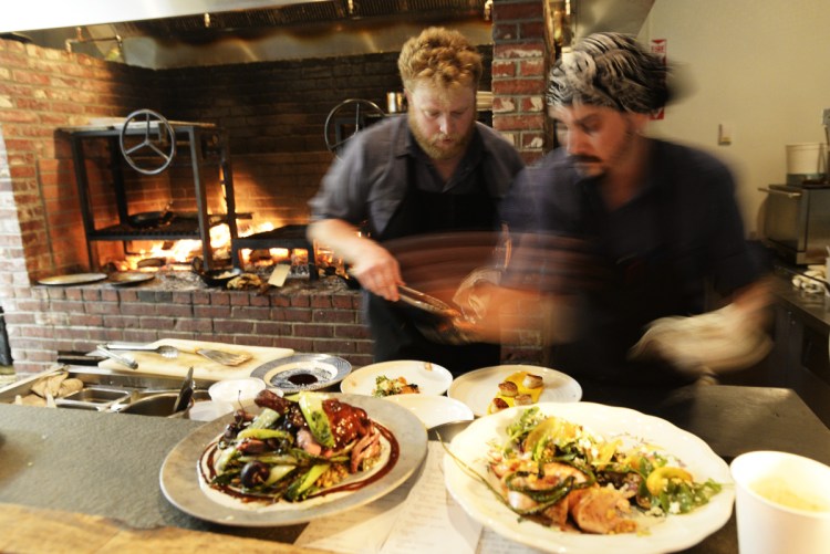 Cooks Matt Jauck, left, and Sean Kach prepare plates in the Walkers Maine kitchen. Chef/owner Justin Walker said the fireplace hearth burns through a cord of wood per week.