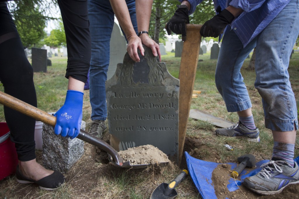 Members of Spirits Alive, a nonprofit group formed 11 years ago to restore and preserve the cemetery, reset a gravestone Saturday after restoring it and reuniting it with the footstone, which was recently recovered near the Dead House.