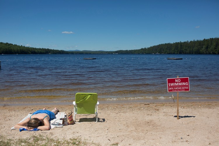 Christy Dow sunbathes on Woods Pond Beach next to one of the no swimming signs that line the sand. Dow, of Naples, said she didn't know about the swimming ban until she saw the sign and said she had driven by the beach in hopes of sunbathing on Thursday, but decided it was too busy. 