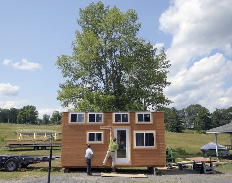 Pat Sirois removes a sign Monday from the tiny home built with sustainable Maine wood products at his home in Litchfield, as Brendell Martin prepares to load the home onto a trailer for a Make-A-Wish recipient.