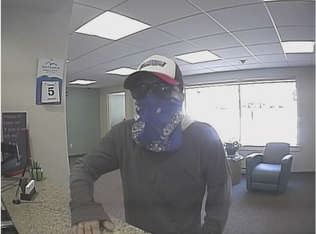 The suspect in the hold up of Bar Harbor Bank and Trust on Route 3 in South China is described as a white male about 5 feet 3 inches with dark hair, dark eyebrows and a slim build. He wore a dark gray longsleeve shirt, dark blue jeans, a blue bandanna, black sunglasses, dark sneakers and a black-and-white baseball hat with a red bill.