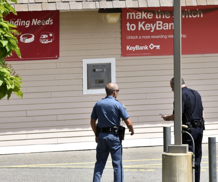 A state trooper, left, and Waterville Sgt. David Caron confer on Tuesday outside the KeyBank branch on Kennedy Memorial Drive in Waterville while investigating a robbery there. Police, guided by dispatchers tracking a GPS device secreted in the stolen money, immediately established a perimeter surrounding the position of the suspect and then tightened the loop around him.