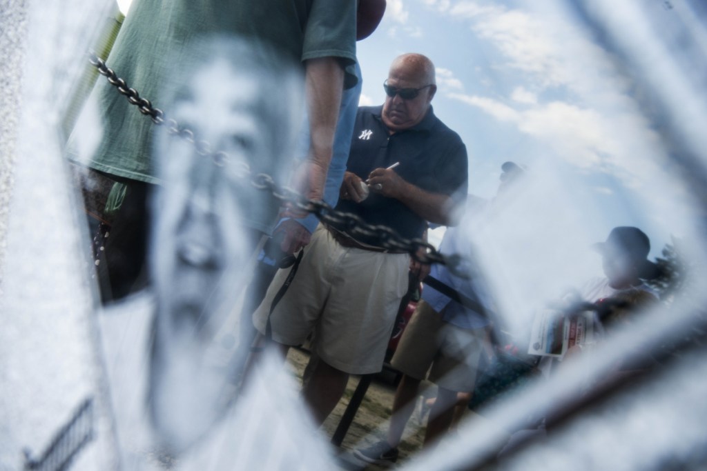 Former New York Yankees manager Stump Merrill signs autographs as he is reflected in a honorary plaque during opening ceremonies for the Cal Ripken 12U New England regional tournament Friday at Purnell Wrigley Field in Waterville.