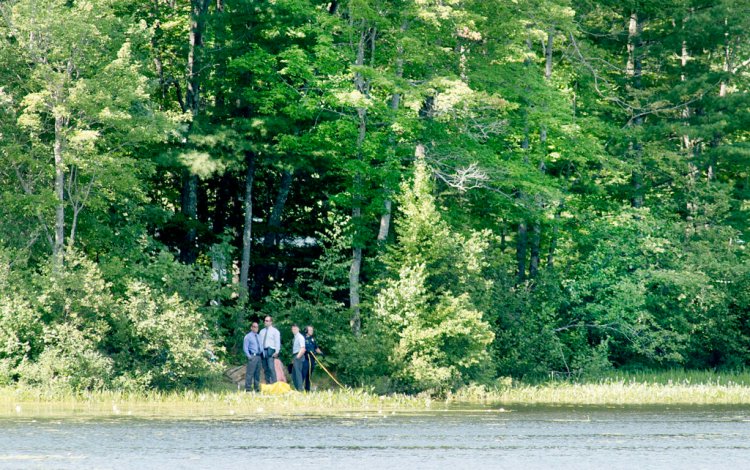 Officers with the Auburn Police Department and the Maine State Police Major Crime Unit investigate a death after a body was discovered near the shoreline of The Basin along Holbrook Road in Auburn on Sunday morning. A diver is being assisted by the officer at right with a yellow line.