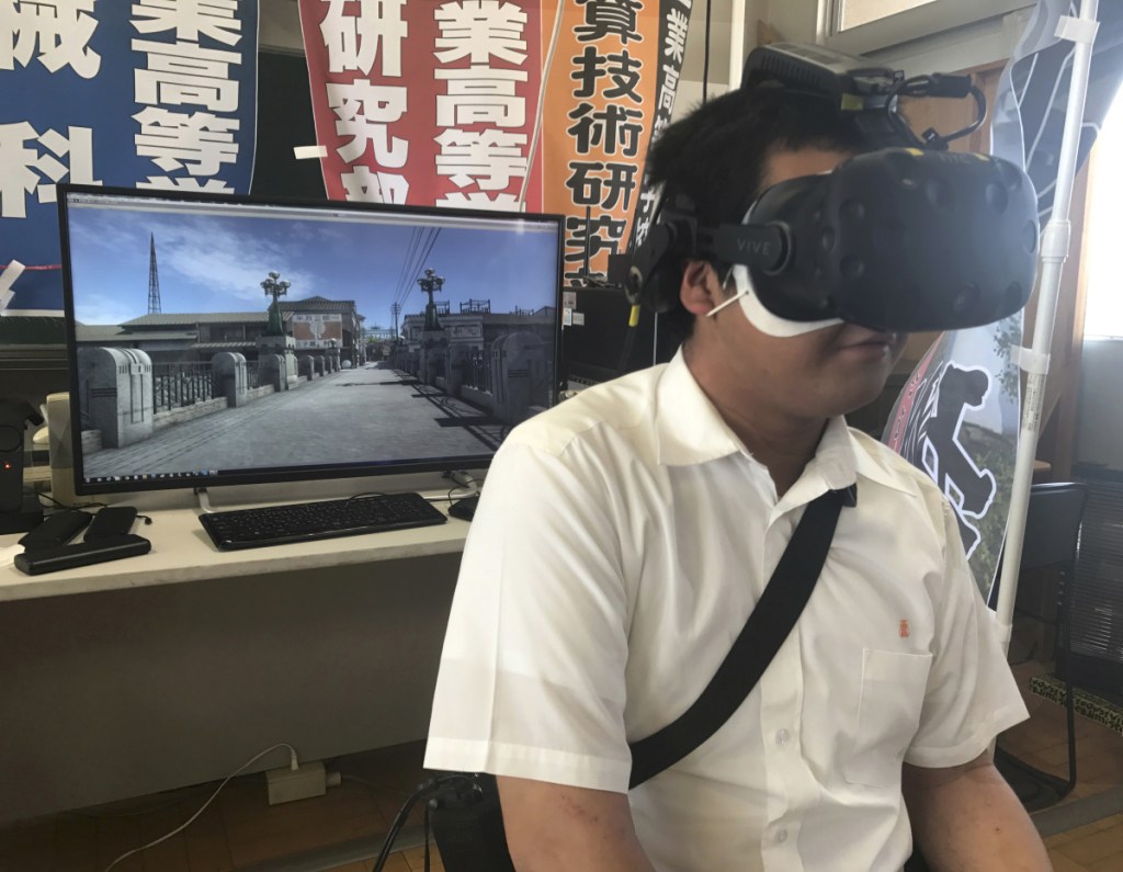 In Friday, Aug. 8, 2018, photo, Namio Matsura, a 17-year-old member of the computation skill research club at Fukuyama Technical High School, watches the bridge over the Motoyasu River, seen on screen, before atomic bomb fell on Hiroshima in virtual reality experience at the school in Hiroshima, western Japan. Over two years, the group of Japanese high school students has been painstakingly producing a five-minute virtual reality experience that recreates the sights and sounds of Hiroshima before, during and after the U.S. dropped an atomic bomb on the city 73 years ago. (AP Photo/Haruka Nuga)