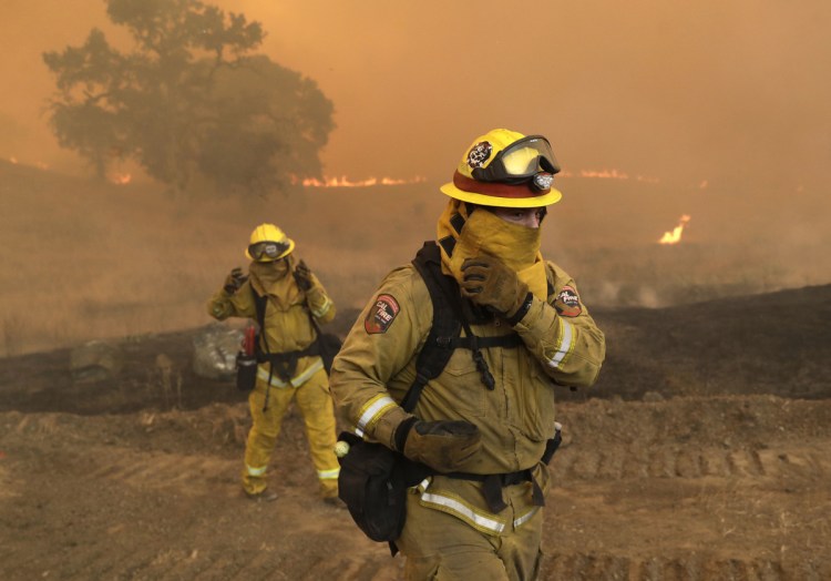 Firefighters with Cal Fire Mendocino Unit cover themselves to protect from smoke and ash created by an advancing wildfire Monday in Lakeport, Calif.