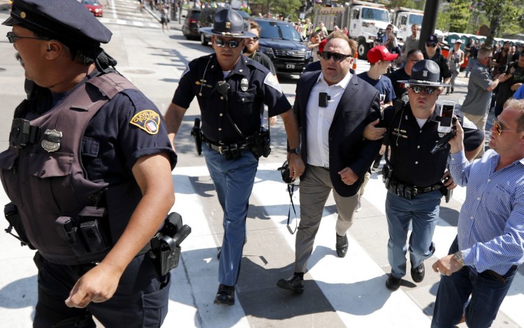 Conspiracy theorist Alex Jones, center right, is escorted by police out of a crowd of protesters outside the Republican National Convention in Cleveland in 2016. Facebook has taken down four pages belonging to Jones for violating its hate speech and bullying policies, but Twitter is leaving his material on its platform.