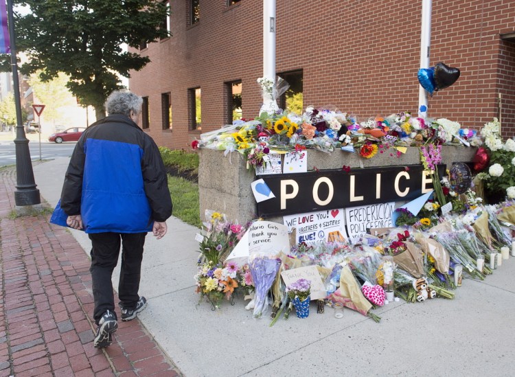 A resident views a makeshift tribute outside the police station in Fredericton on Saturday. Two officers were among four people killed in a shooting in a residential area on the city's north side. 