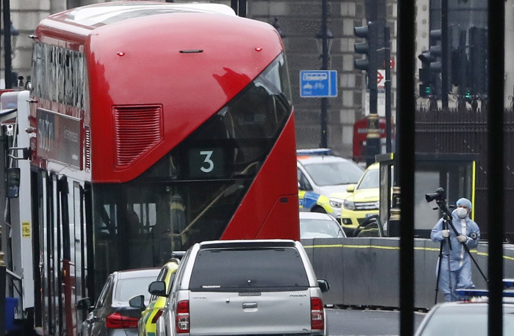 A forensics officers works near the scene near a car that crashed into security barriers outside the Houses of Parliament to the right of a bus in London. London police say the incident is being treated as a terrorist attack.