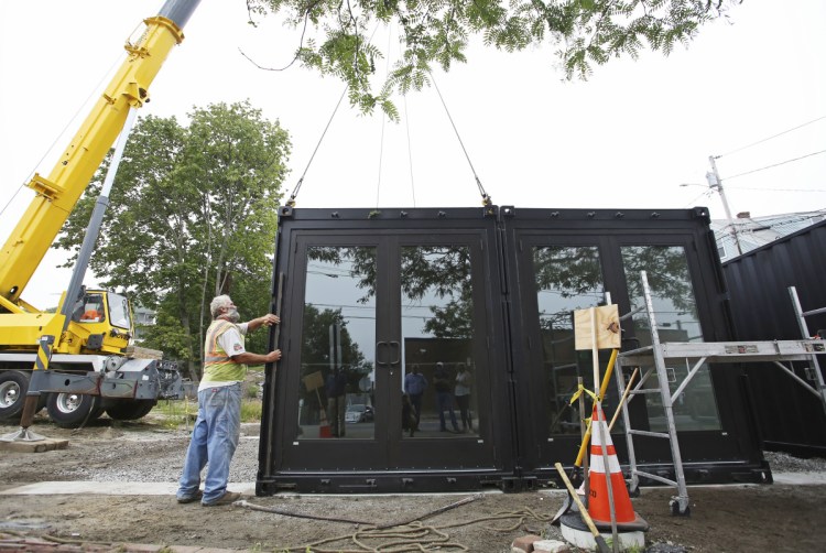 John Anderson uses a level Monday as entry doors are placed on modified shipping containers at 93 Washington St. in Portland. The five containers, pre-built by SnapSpace Solutions in Brewer, will hold five retail storefronts, allowing businesses to experiment without long-term lease commitments.