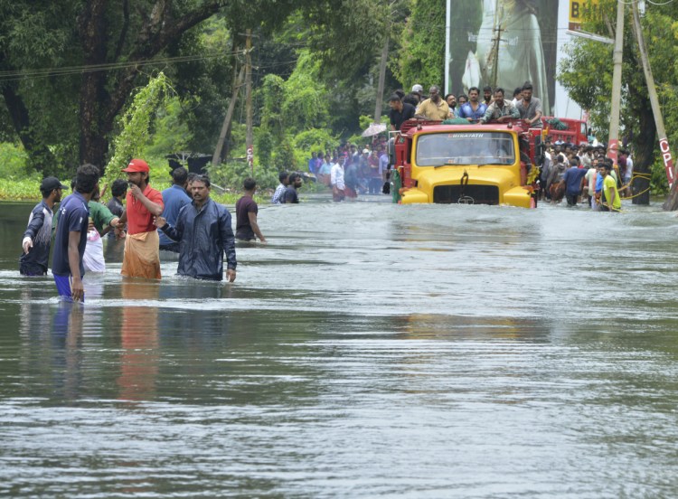 A truck carries people past a flooded road in Thrissur, in the southern Indian state of Kerala, on Saturday. Rescuers used helicopters and boats Friday to evacuate thousands of people stranded on their rooftops from the  flooding.