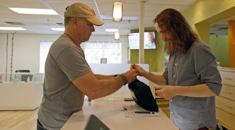 Scott Durst, left, retired from the Maine Drug Enforcement Agency, receives a deposit bag of cash from Kyle Dunn, manager of Wellness Connection, a dispensary in Portland.