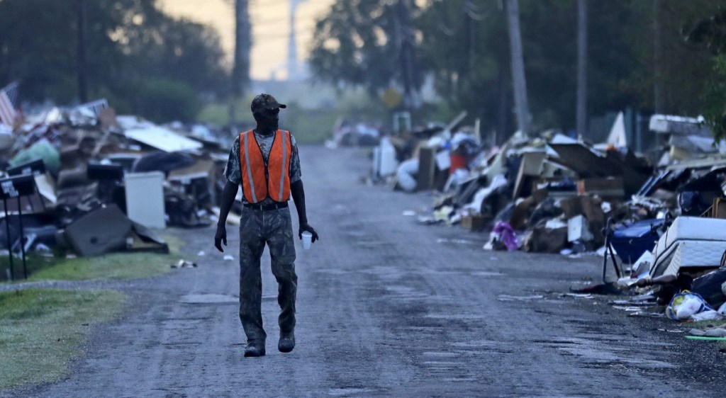 FILE - In this Sept. 28, 2017, file photo, a man walks past debris from homes on his street damaged in flooding from Hurricane Harvey as an oil refinery stands in the background in Port Arthur, Texas. Although many Texas families are still struggling to recover from Hurricane Harvey a year after it caused widespread damage and flooding along the Gulf Coast and in and around Houston, daily life has mostly returned to normal in many of the hardest hit communities. (AP Photo