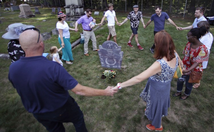 The family of Walter Skold, founder of the Dead Poets Society of America, dance and sing around his grave at Pine Grove Cemetery in Brunswick on Monday. Skold died of a heart attack after enlisting the son of novelist John Updike to carve a unique grave marker.