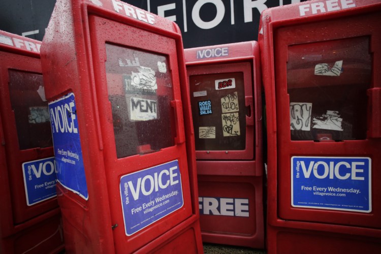 In this Nov. 27, 2013, photo, plastic newspaper boxes for The Village Voice stand along a Manhattan sidewalk in New York. Village Voice publisher Peter Barbey announced Friday that the venerable alternative weekly will cease publication. The announcement comes three years after Barbey bought the paper and one year after it ceased publishing in print.