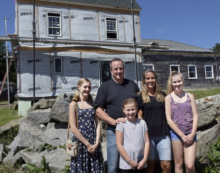 Calista, left, Christina and Shae-Lynn Pagurko with their parents, John and Melanie, are seen outside the home they are rebuilding on Thursday in Whitefield following a destructive fire last year.