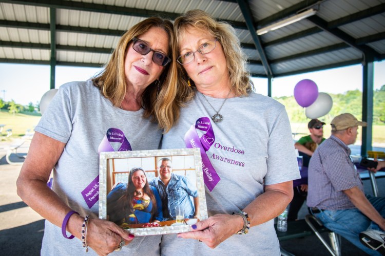 Louise Atkinson, left, of West Gardiner, and Sharon Bailey, of Jefferson, hold a photo of their children, Jessica and Matt, who were engaged to be married and died within six months of each other from drug overdoses. The mothers organized of a grief recovery group to help others who lost someone to substance use at an event in Mill Park in Augusta on Friday.