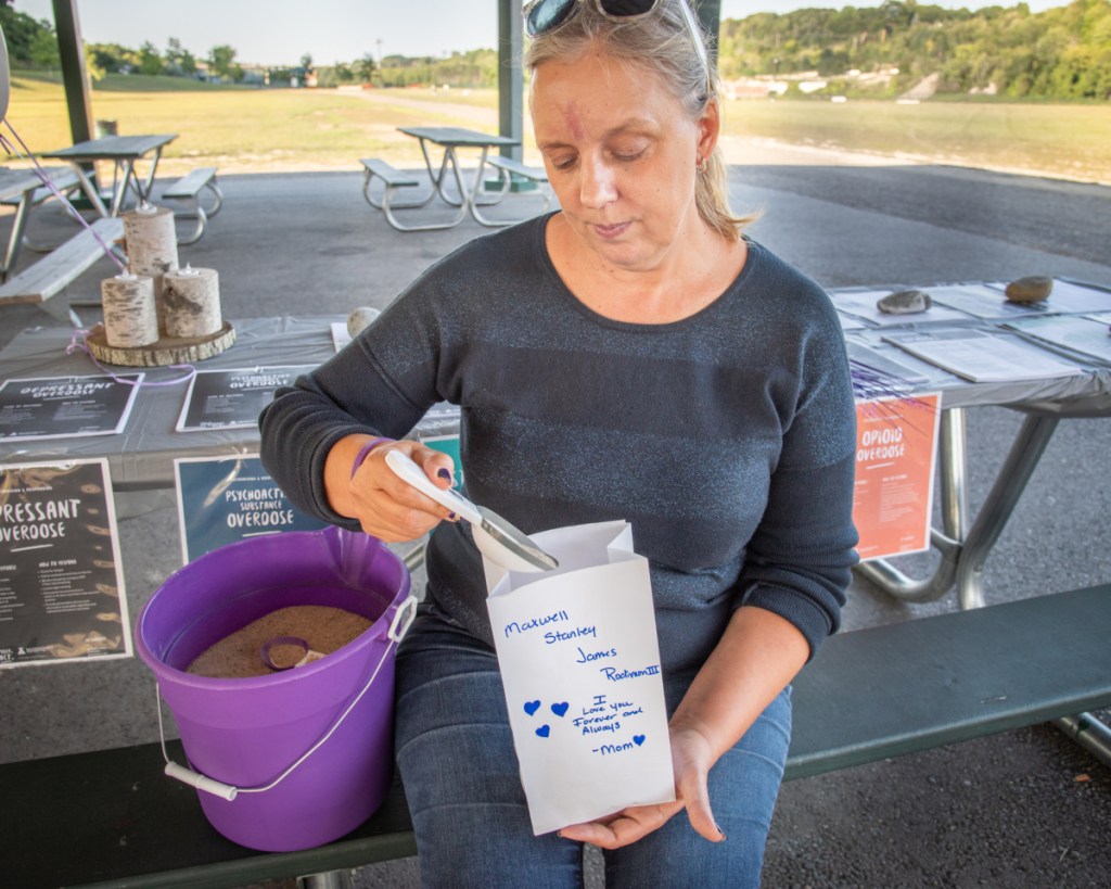 Mary Rodimon, of North Yarmouth, fills a luminary bag with sand, which she dedicated to her son Max, who died from a drug overdose in June. Rodman attended an event organized by GRASP, Grief Recovery After a Substance Passing, at Mill Park in Augusta on Friday.