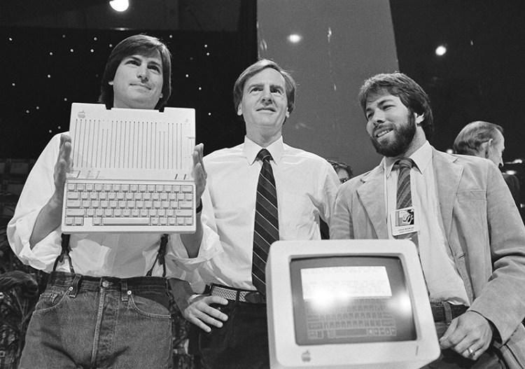 FILE - In this April 24, 1984 file photo, Steve Jobs, left, chairman of Apple Computers, John Sculley, center, president and CEO, and Steve Wozniak, co-founder of Apple, unveil the new Apple IIc computer in San Francisco, Calif.  Apple has become the world’s first company to be valued at $1 trillion, the financial fruit of tasteful technology that has redefined society since two mavericks named Steve started the company 42 years ago.  Associated Press/Sal Veder