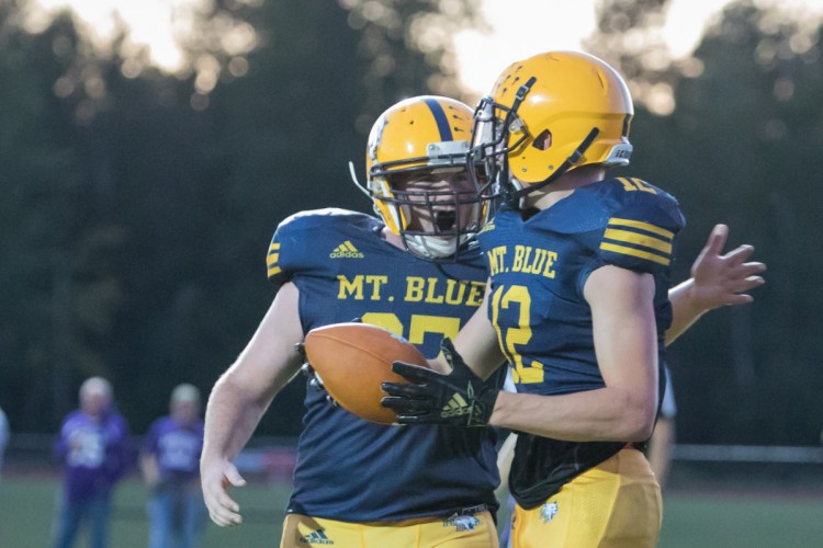 Mt. Blue's Dakota Mumma, left, celebrates with Randy Barker after Barer scored a touchdown during a Pine Tree Conference Class B game Friday night against Hampden at Caldwell Field in Farmington.