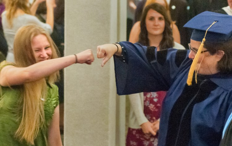 Rising Scholar Jacinta Hunt, left, and Lorien Lake-Corral, the professor who nominated her, bump fists Friday as they part company during the entrance processional at the annual University of Maine at Augusta convocation at the Augusta Civic Center.