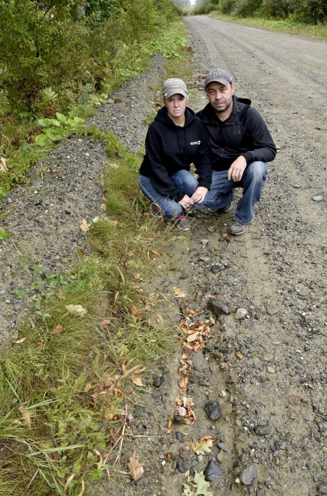 Albion residents Leanne York and Robert Brown crouch next to the rutted Marks Road on Tuesday to show that the road's shoulder is considerably higher than the roadway and prevents water from running off the road surface. Brown said he has complained to town officials about it since 2016.