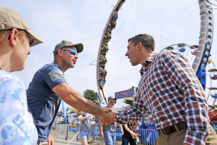 Zak Ringelstein, 32, at right, greets Jason Hoffman of Florida and Anita Perkins of Atkinson at the Skowhegan State Fair. Ringelstein hopes to capitalize on the energy stirred up by young politicians like Alexandria Ocasio-Cortez of New York. 