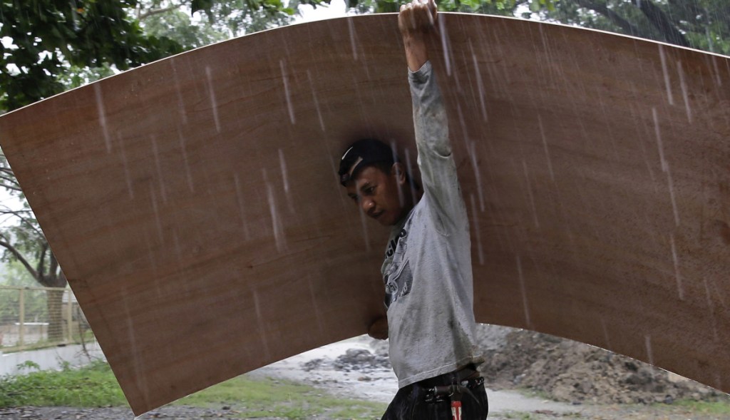 A worker uses a sheet of plywood to cover himself from the rain as Typhoon Mangkhut nears the northeastern Philippines on Friday.