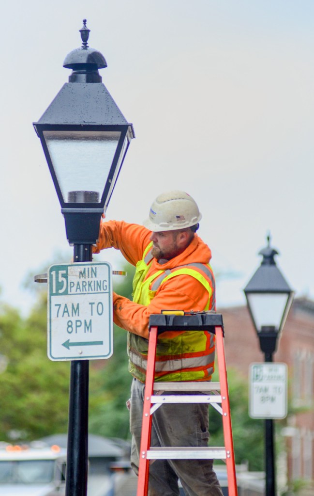 Dan Clark, of Sargent Corporation, installs 15 minute parking signs on new lamp posts on Tuesday on Water Street in downtown Hallowell. The road will open to two-way traffic again on Friday afternoon after a months-long reconstruction project.