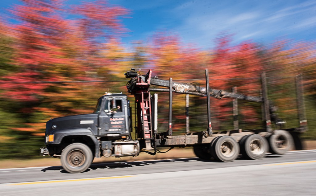 An empty logging truck zooms past a large display of autumn foliage Friday afternoon on Route 26 in Woodstock.