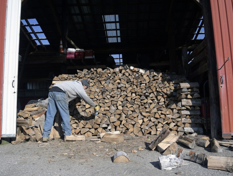 Rick Carmichael stacks firewood Tuesday in a shed at E.C. Barry & Son in Farmingdale. The firewood dealer uses the wood to heat the offices at the business.