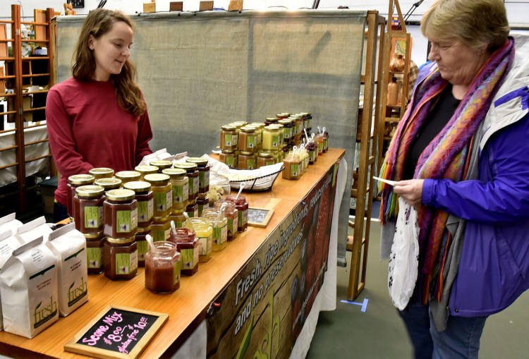 Kaitlin Volk, left, of Fresh Harvest in a Jar, waits as Deb Bomaster chooses a jam to sample Sunday during the REM Craft Fair in Waterville.