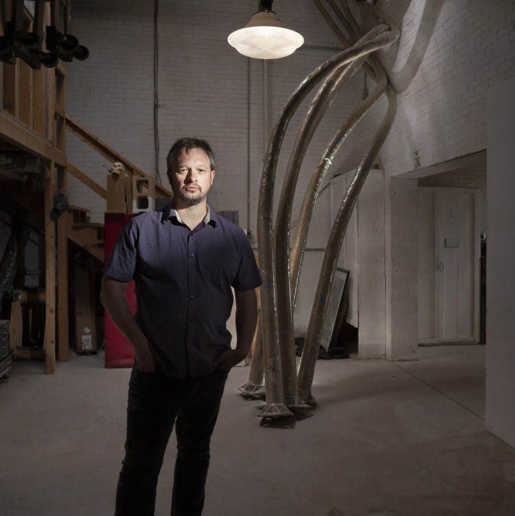 Aaron Stephan poses with the curved poles of his sculpture  "Luminous Arbor" in his Portland studio Wednesday. 