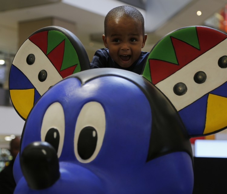 A child looks over the head of a Mickey Mouse statue at an exhibition at Sandton City in Sandton, South Africa, Sunday.