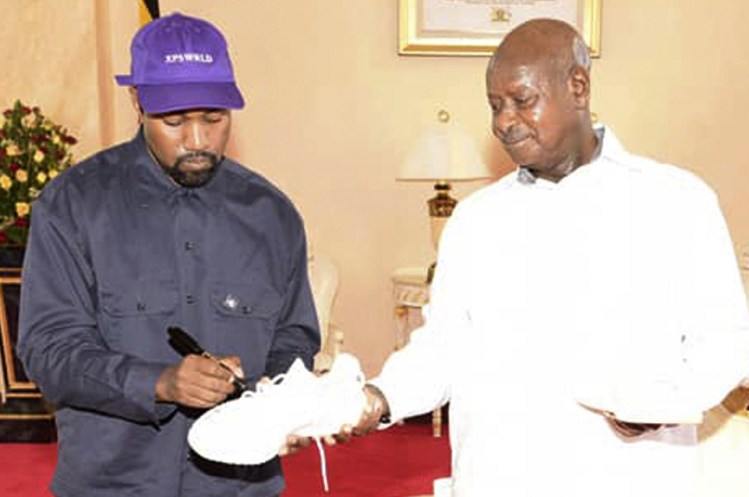 Kanye West autographs a pair of his sneakers Monday as a gift to Uganda's President Yoweri Museveni at the State House in Entebbe, Uganda. Museveni said he and West held "fruitful discussions" about promoting tourism and arts in the East African nation in which the rapper is said to be recording music in a tent.