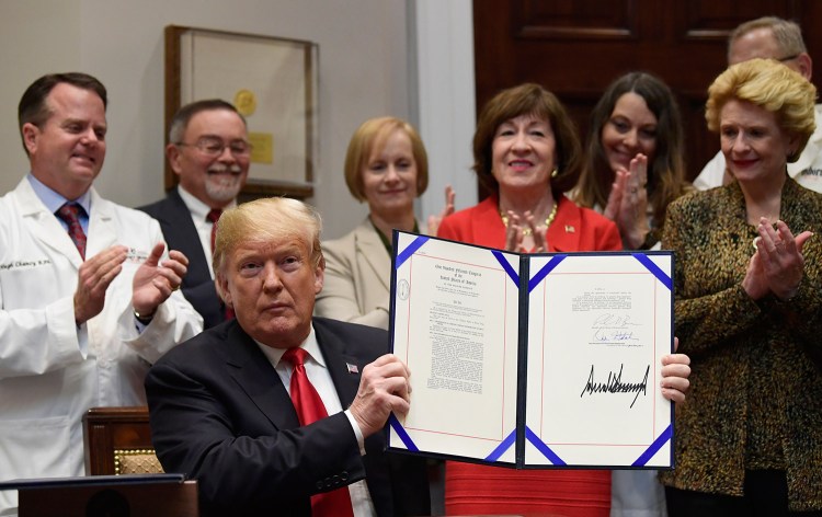President Trump holds up the "Patient Right to Know Drug Prices Act" after signing it and the "Know the Lowest Price Act of 2018," during a ceremony at the White House in Washington on Wednesday. The bills, which were sponsored by Sen. Susan Collins, R-Maine, at rear, and Sen. Debbie Stabenow, D-Mich., right, help protect Medicare patients and those with private insurance from overpaying for prescription drugs by outlawing pharmacy "gag clauses." 
