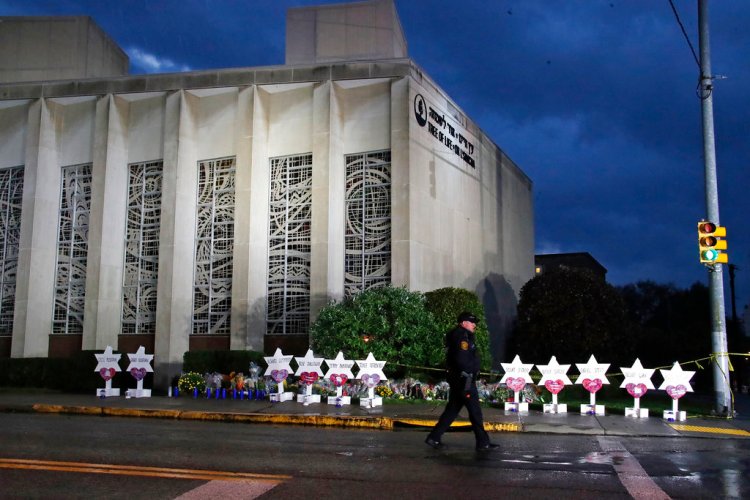A Pittsburgh Police officer walks past the Tree of Life Synagogue and a memorial of flowers and stars in Pittsburgh on Sunday, in remembrance of those killed and injured when a shooter opened fire during services Saturday at the synagogue. 