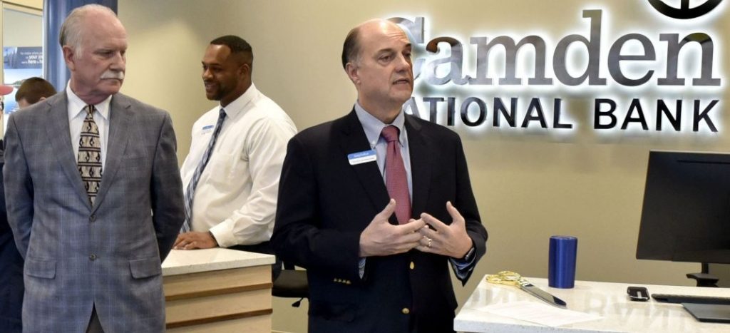 As customer Donna Goggin is assisted by teller Alex Green, Camden National Bank President and CEO Greg Dufour, right, and Chairman of the Board Larry Sterrs speak during a grand opening of the bank in the Bill & Joan Alfond Main Street Commons building in Waterville on Monday.
